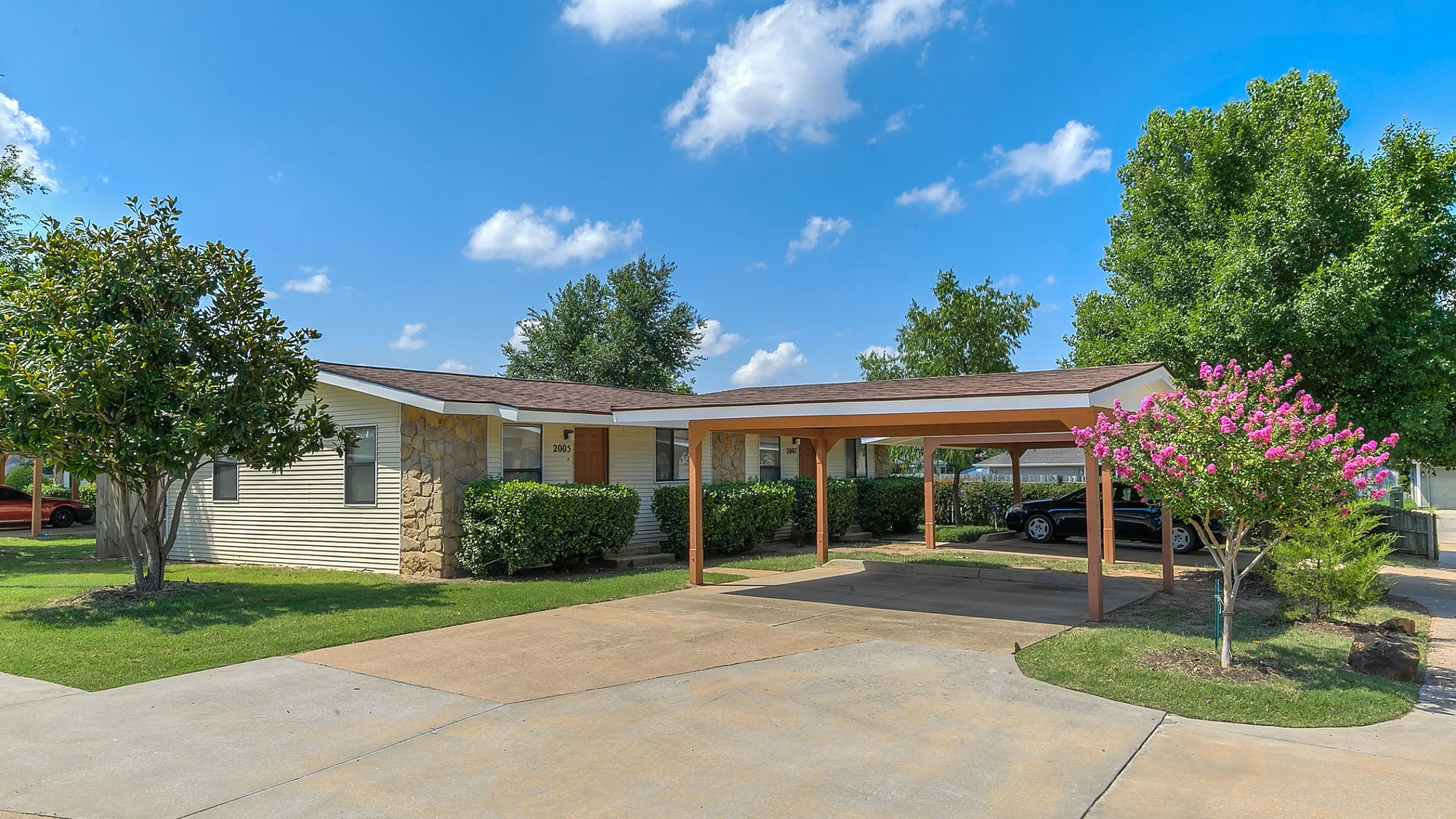 Inviting suburban home with carport, surrounded by lush greenery and a vibrant flowering tree.