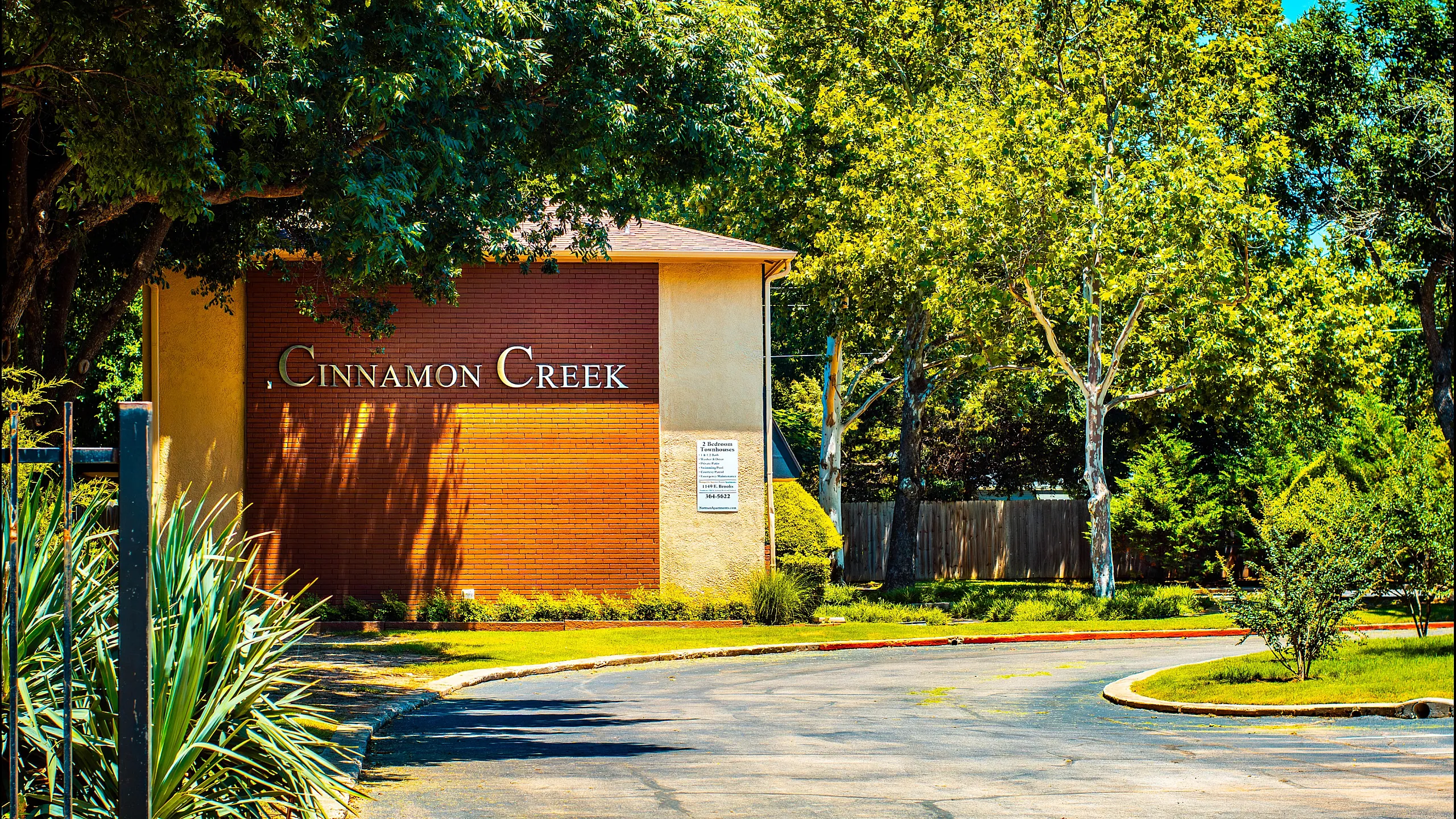 Inviting entrance of Cinnamon Creek apartment complex surrounded by lush greenery.