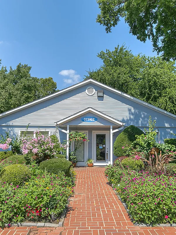 Beautiful entrance of an office surrounded by vibrant, lush gardens and a red brick walkway.