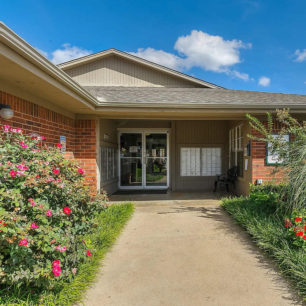 Welcoming apartment entrance surrounded by vibrant landscaping and blooming flowers under a clear blue sky.