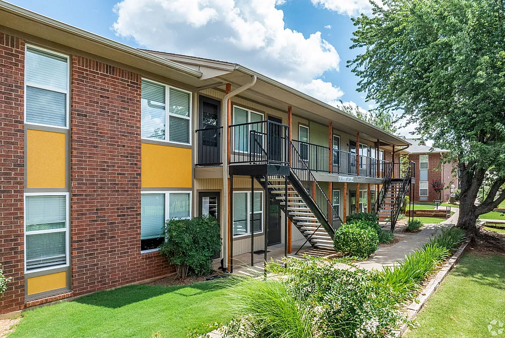 Charming apartment complex with a vibrant exterior, featuring lush landscaping and modern staircases under a bright blue sky.