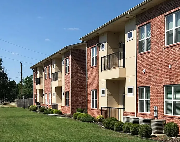 Charming brick apartment complex with lush green lawn and modern design, offering a serene and inviting living environment.