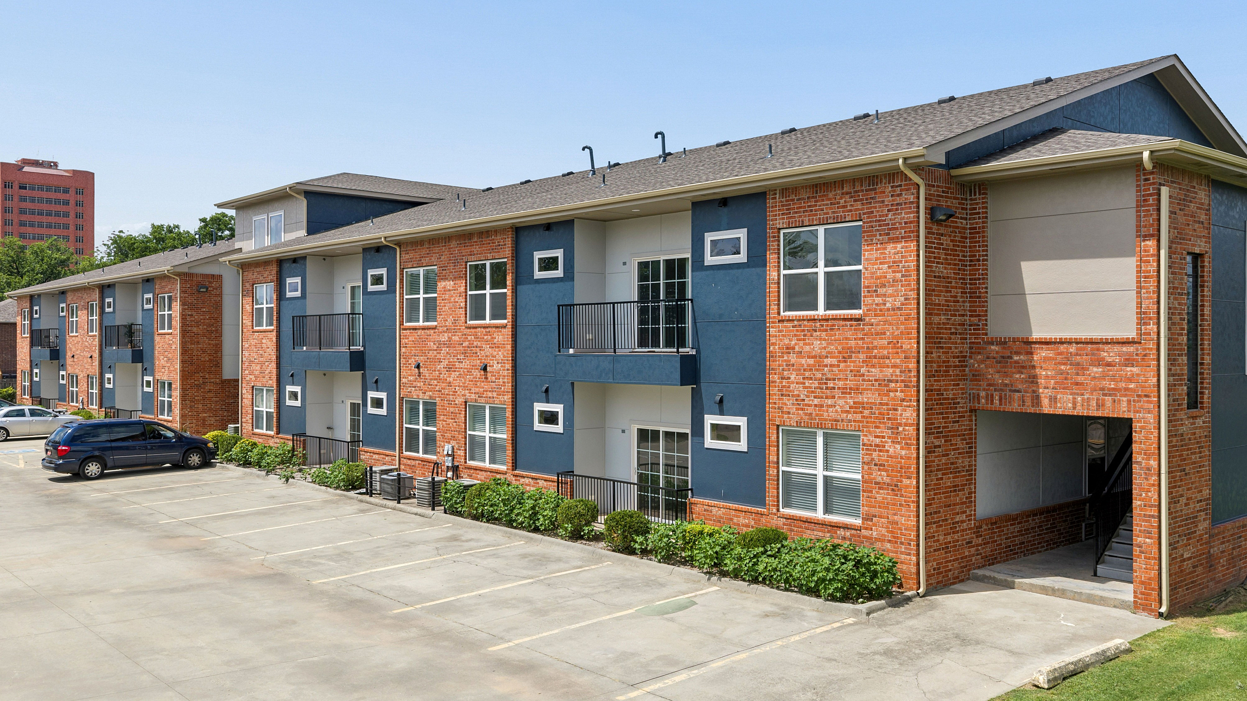 Modern brick and blue facade apartment complex with balconies and ample parking.