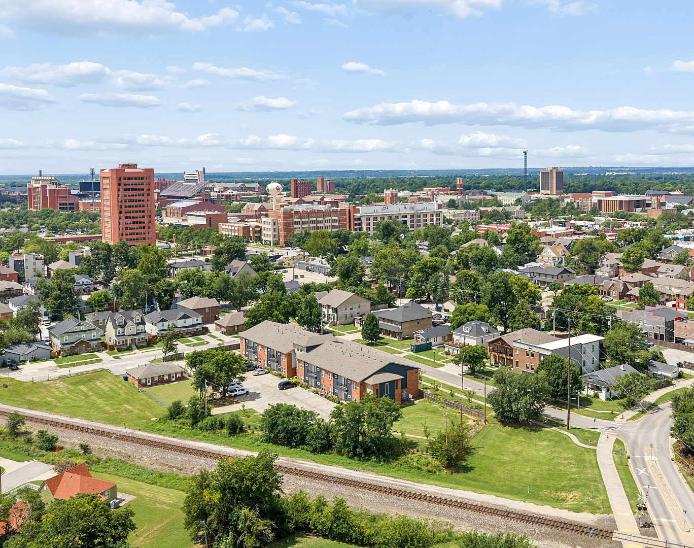 Scenic aerial view of a vibrant urban neighborhood with lush greenery, showcasing charming residential houses and modern buildings under a bright blue sky.