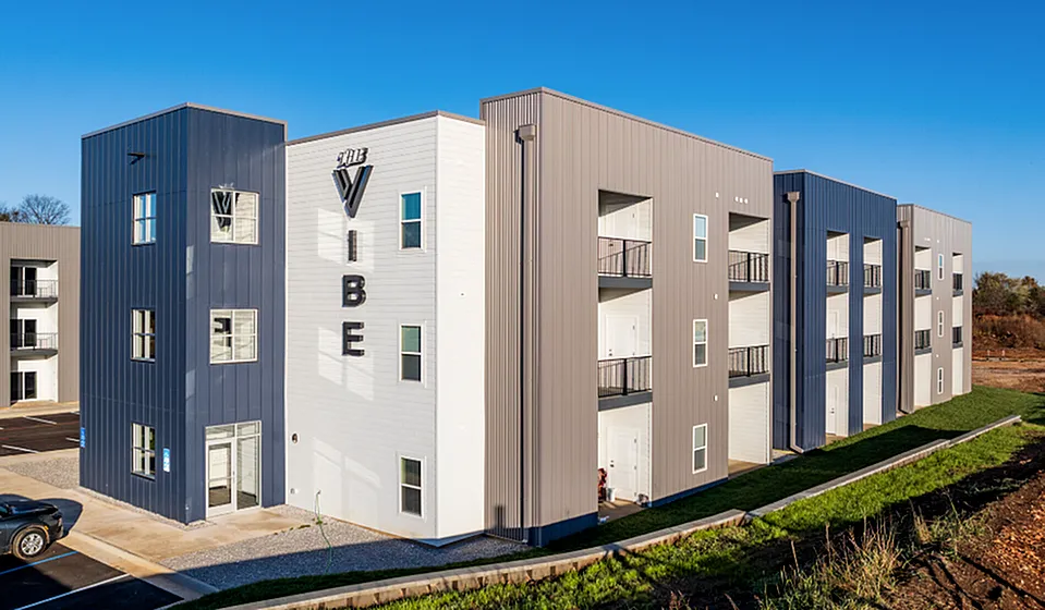Modern apartment building with sleek design, featuring multiple floors, private balconies, and ample natural light, set against a clear blue sky.