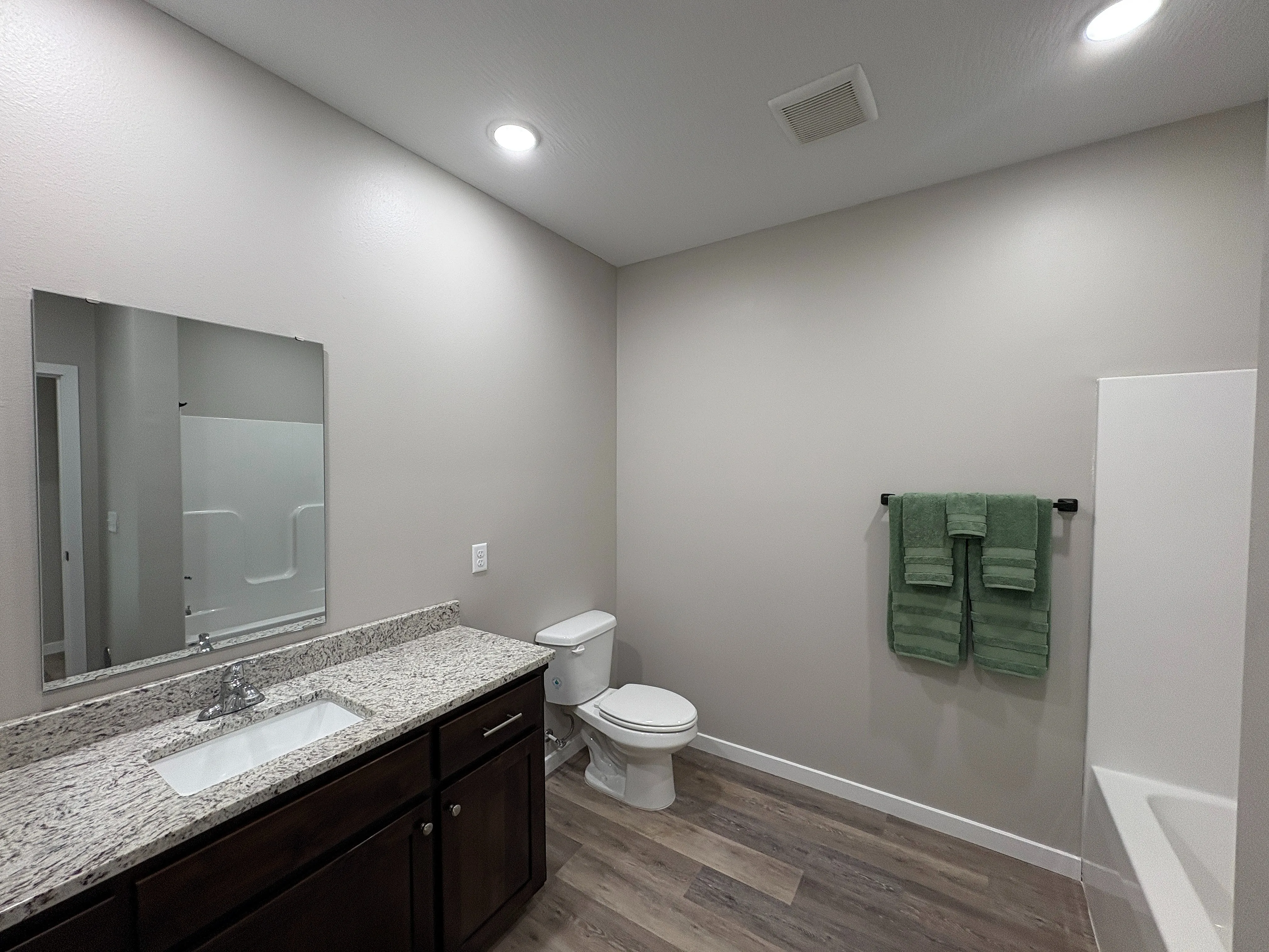Modern bathroom featuring elegant granite countertop, stylish wooden cabinetry, and pristine fixtures under soft lighting.