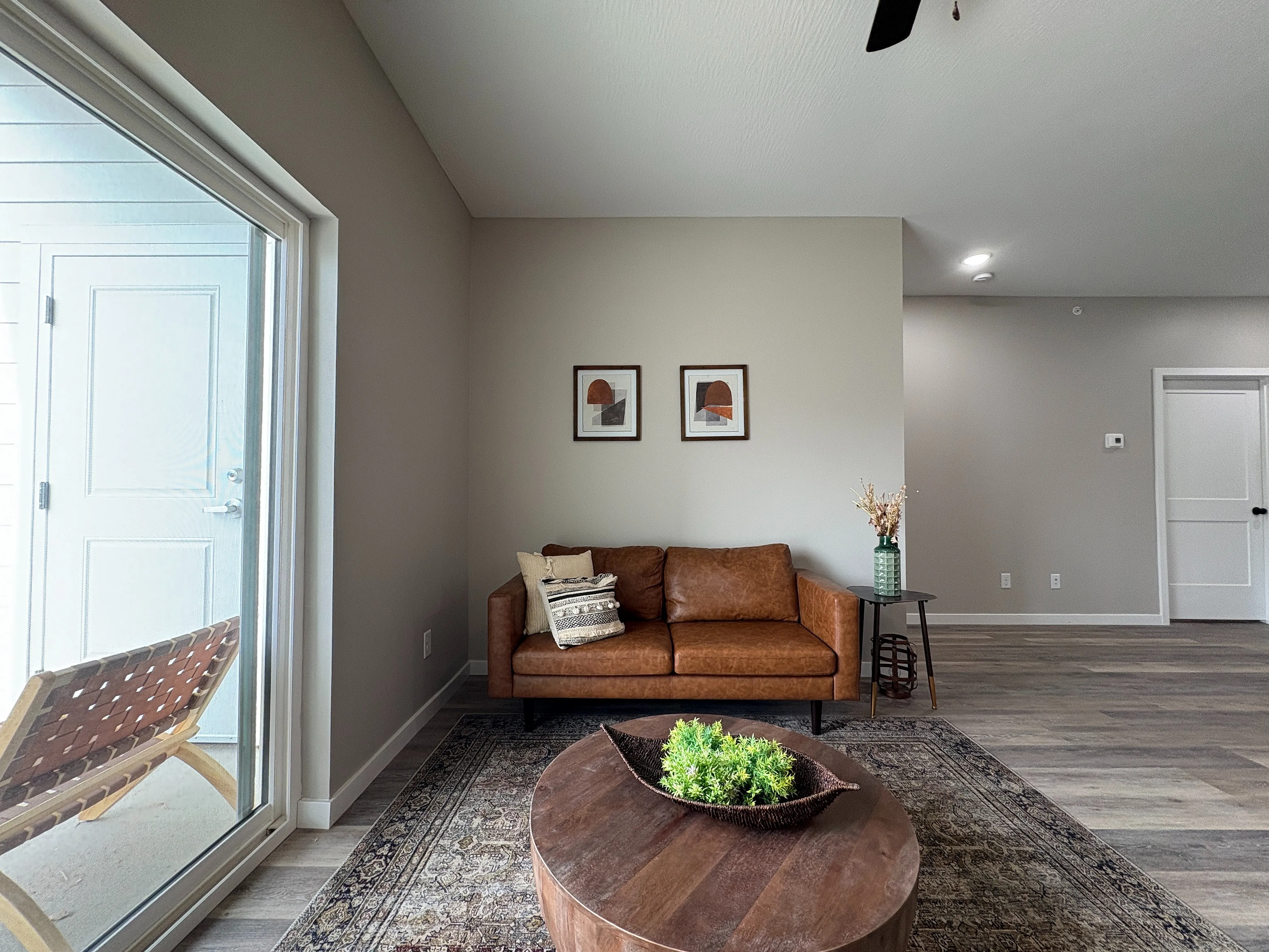 Cozy living space with a stylish leather sofa, modern decor, and natural light pouring in from large glass doors leading to a patio.