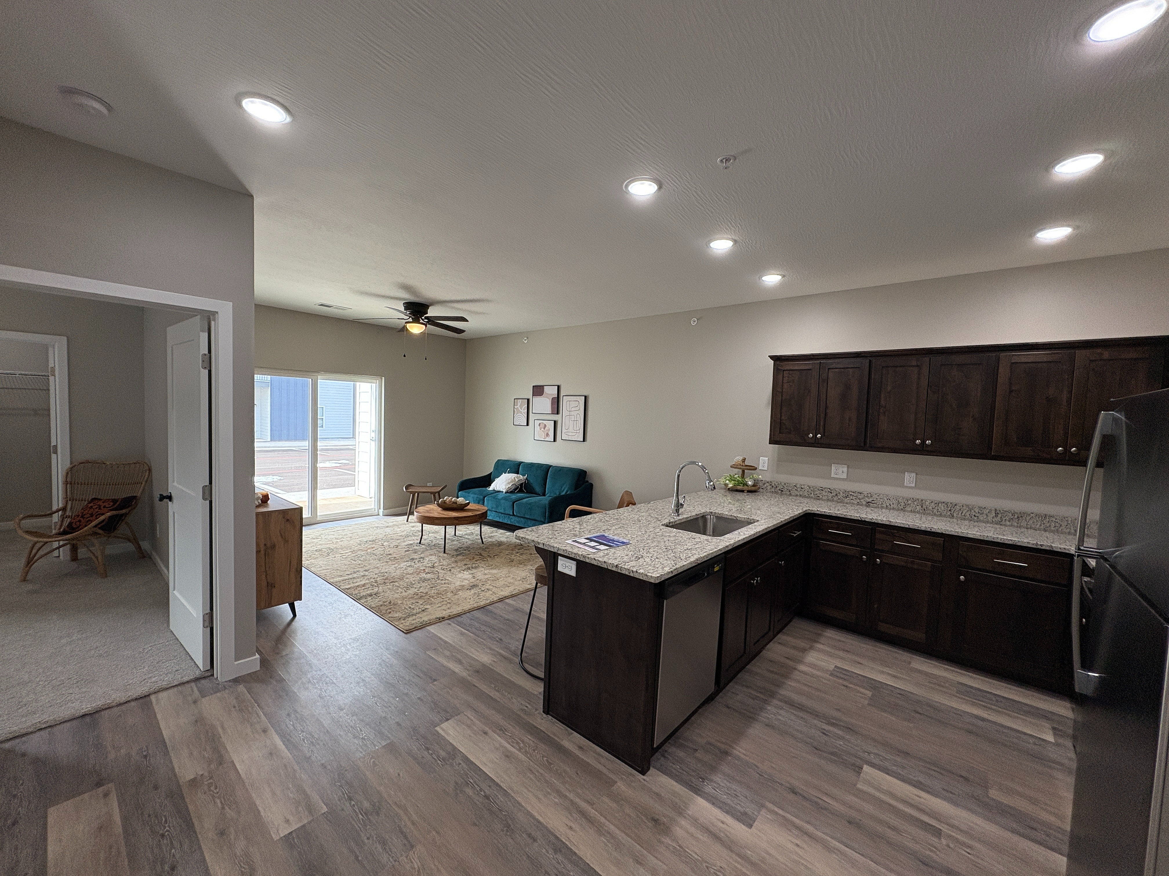 Inviting open-plan living space featuring a modern kitchen with dark wood cabinets, spacious living area with sliding glass doors, and cozy adjacent room.