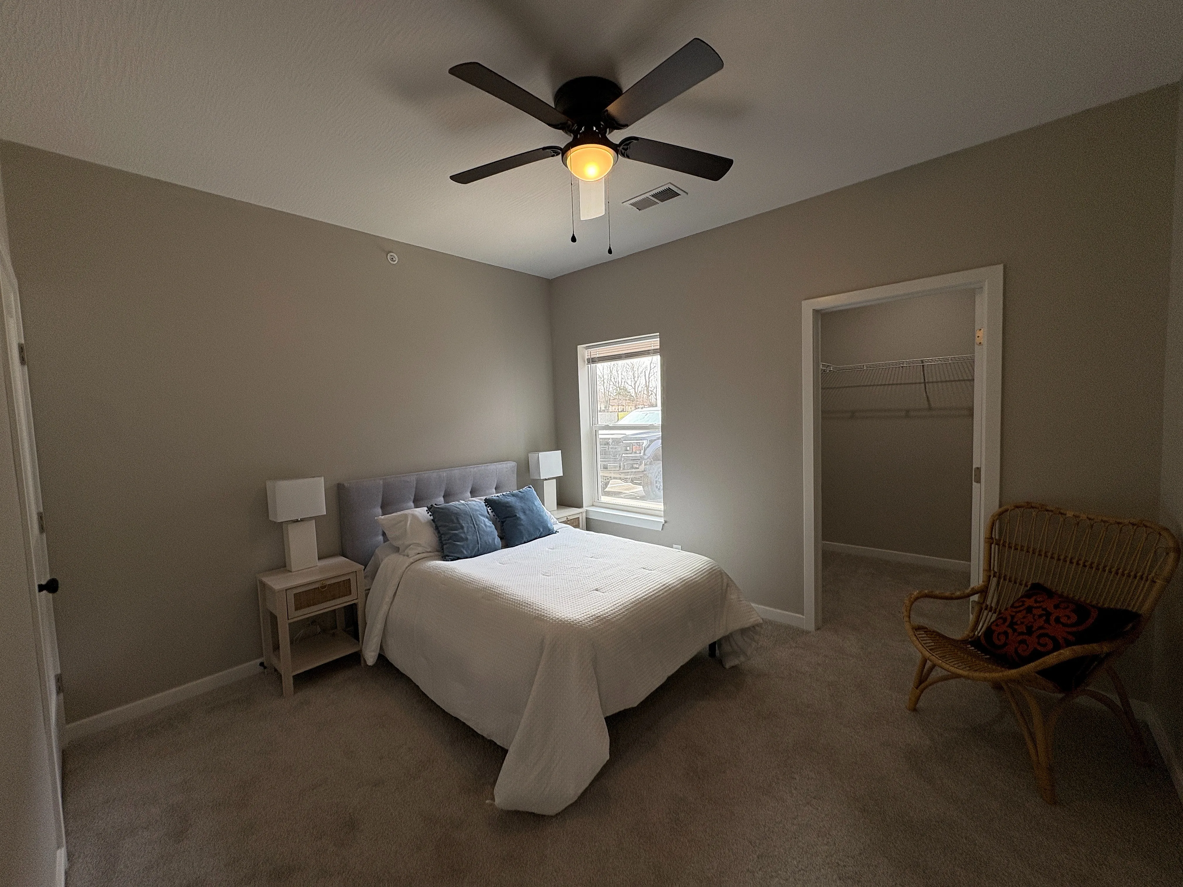 Inviting bedroom with a cozy queen bed, elegant ceiling fan, and a spacious walk-in closet, perfect for modern living.