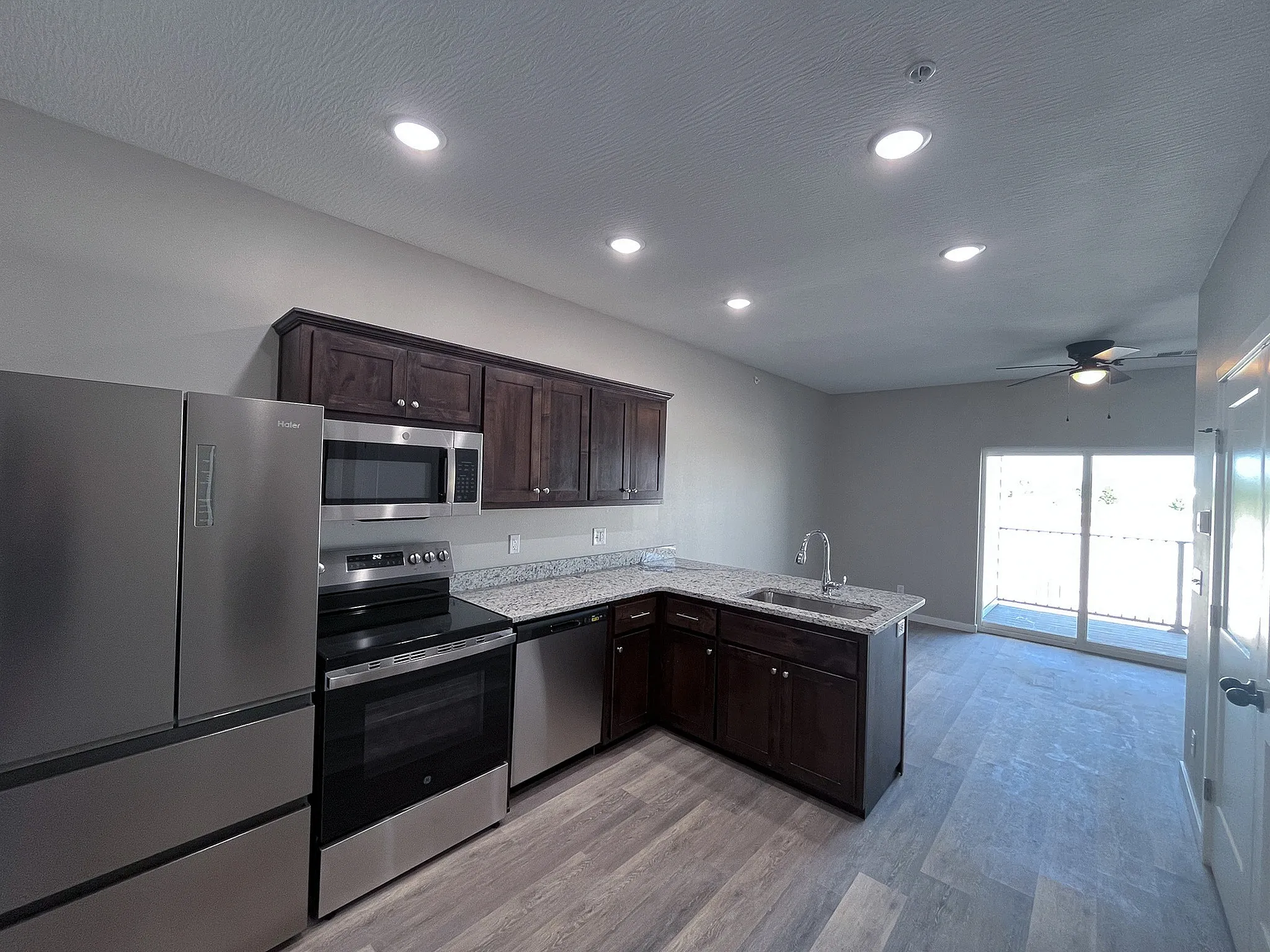 Modern kitchen in open-concept apartment featuring stainless steel appliances, sleek granite countertops, and ample natural light from large sliding glass doors.