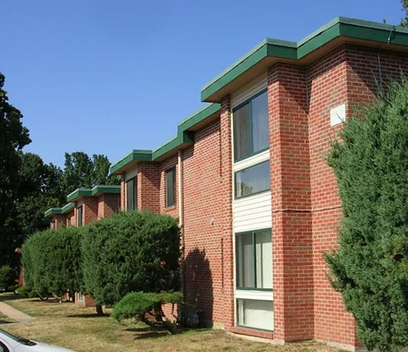 Charming brick apartment complex with lush greenery and large windows, offering a serene living experience.