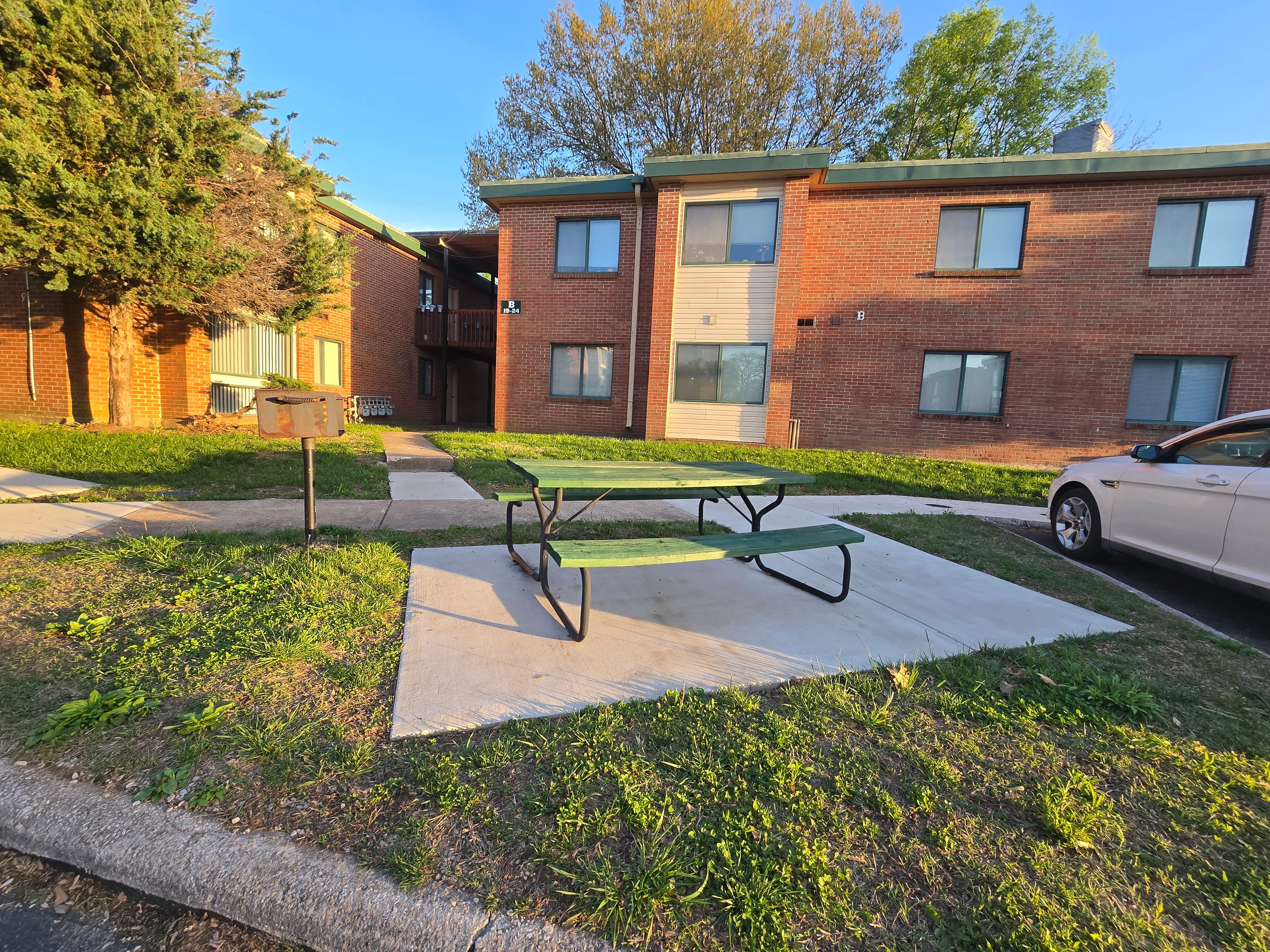 Charming brick apartment complex with lush greenery and picnic area, perfect for outdoor relaxation.