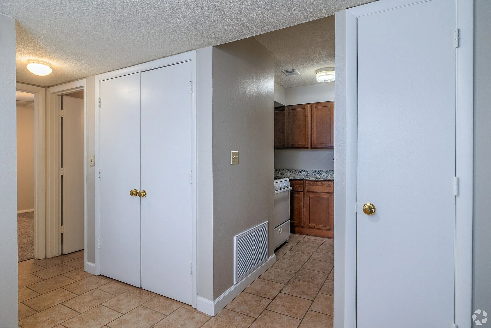 Charming apartment hallway leading to a cozy kitchen with wooden cabinets and sleek tile flooring, featuring ample closet space and ambient lighting.