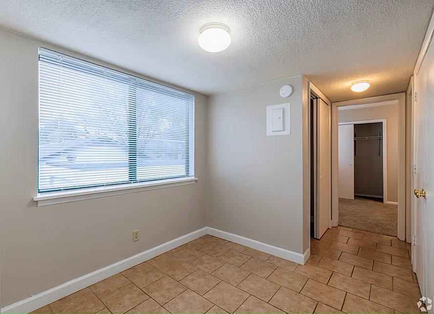 Bright and airy room with large window, tiled floor, and cozy carpeted closet, perfect for a serene living space.
