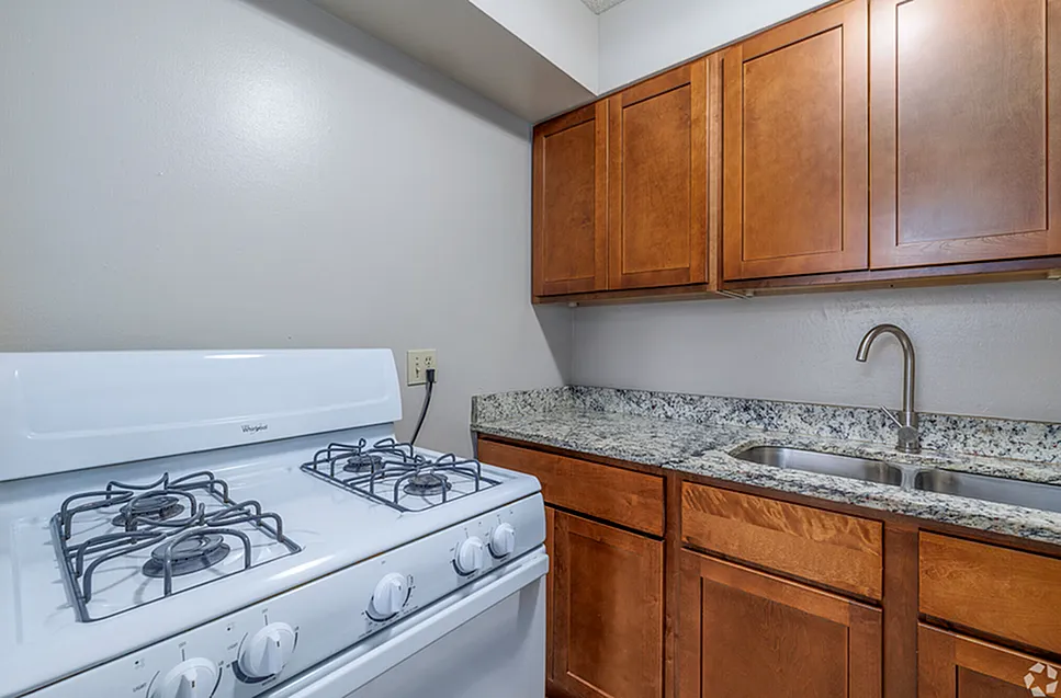 Modern kitchen with sleek granite countertops, wooden cabinets, and a white gas stove.
