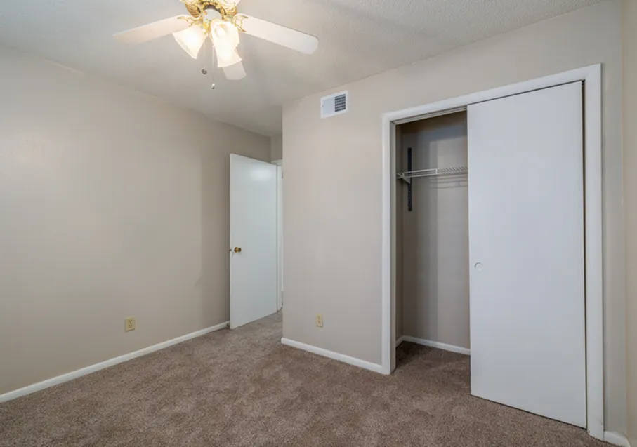 Charming bedroom with soft beige walls, plush carpet, and a cozy closet, featuring a ceiling fan for comfort.