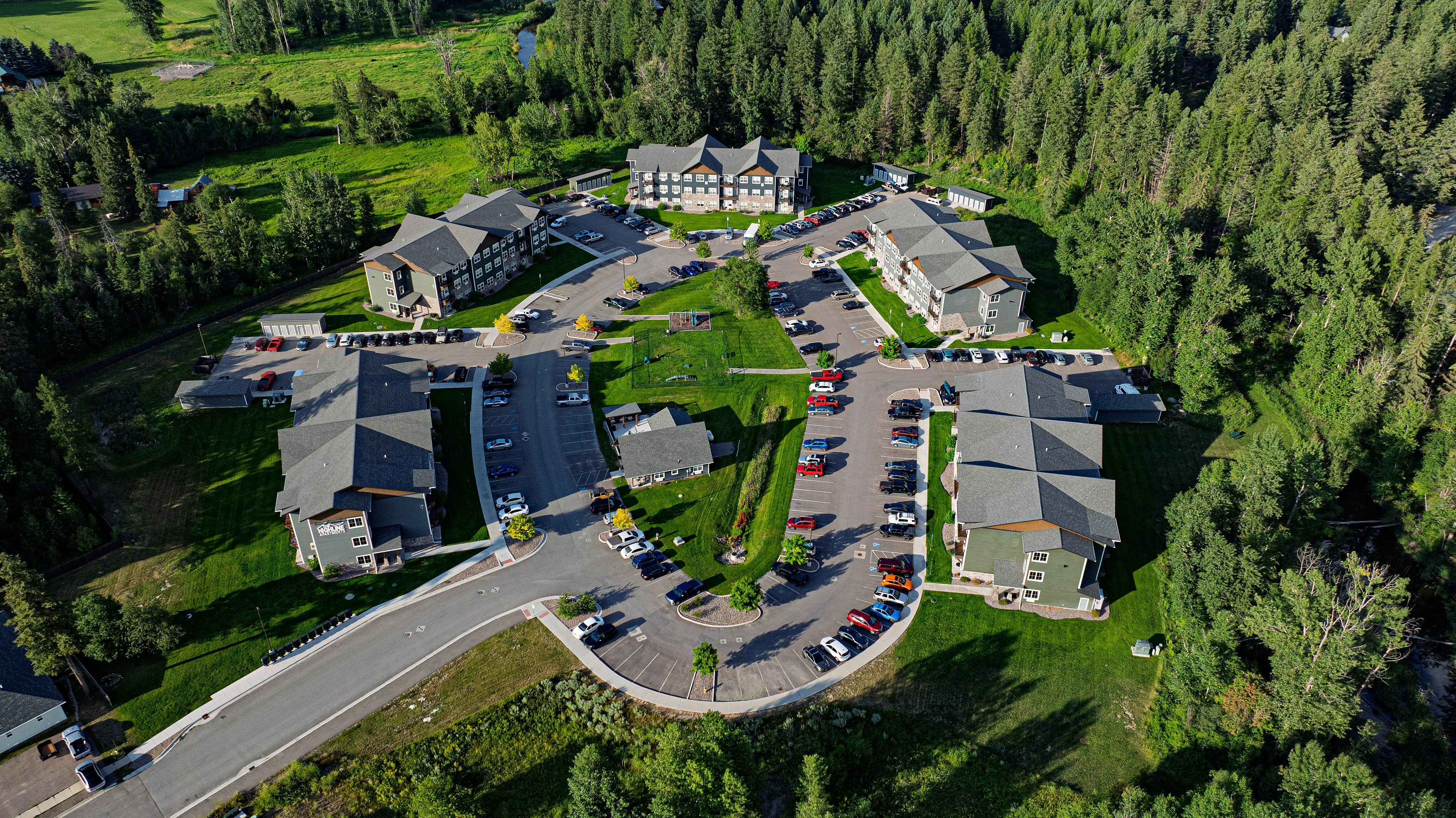 Scenic aerial view of a charming apartment complex nestled in lush greenery, featuring modern buildings, ample parking, and vibrant landscapes.