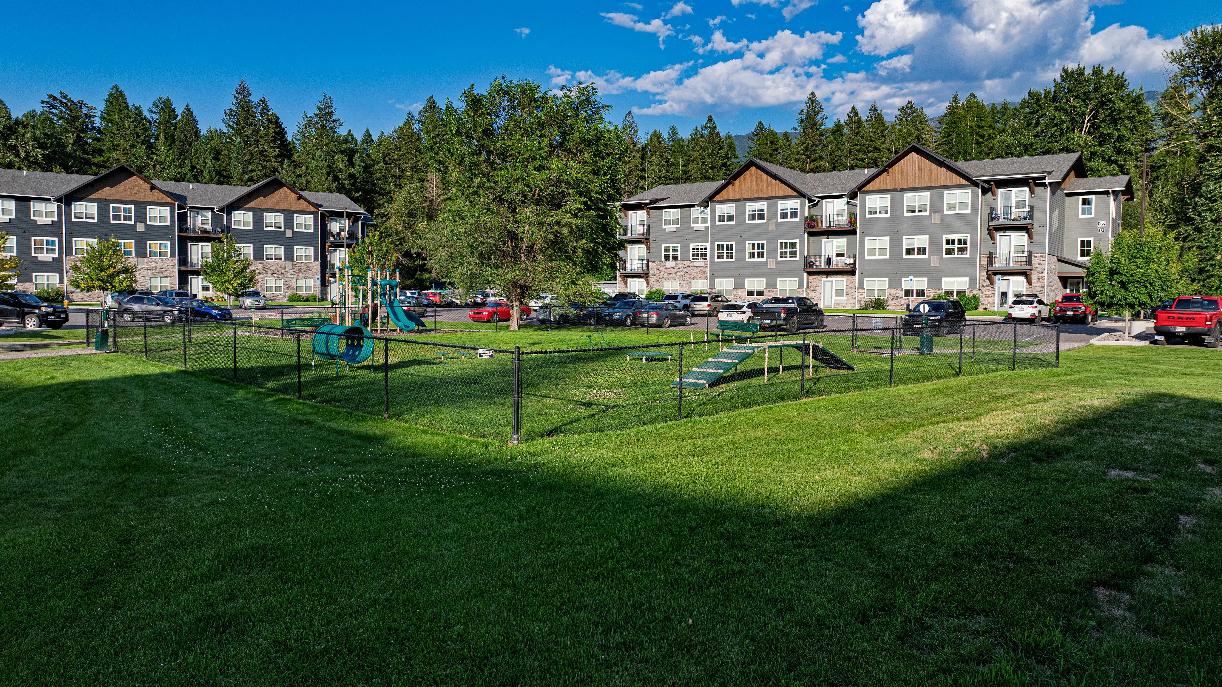 Charming apartment complex with modern design nestled in lush greenery, featuring ample parking and a vibrant playground.