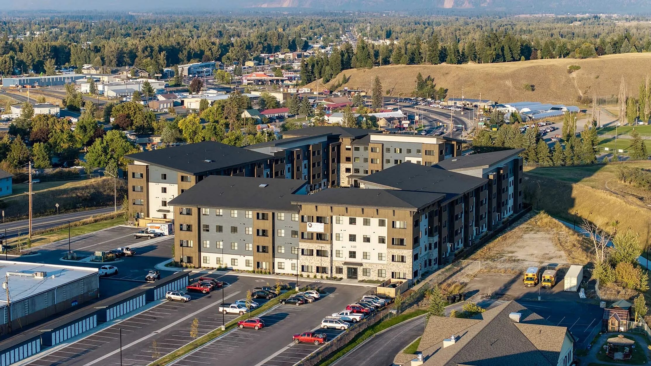Scenic aerial view of modern apartment complex surrounded by lush greenery and rolling hills, offering ample parking and urban convenience.