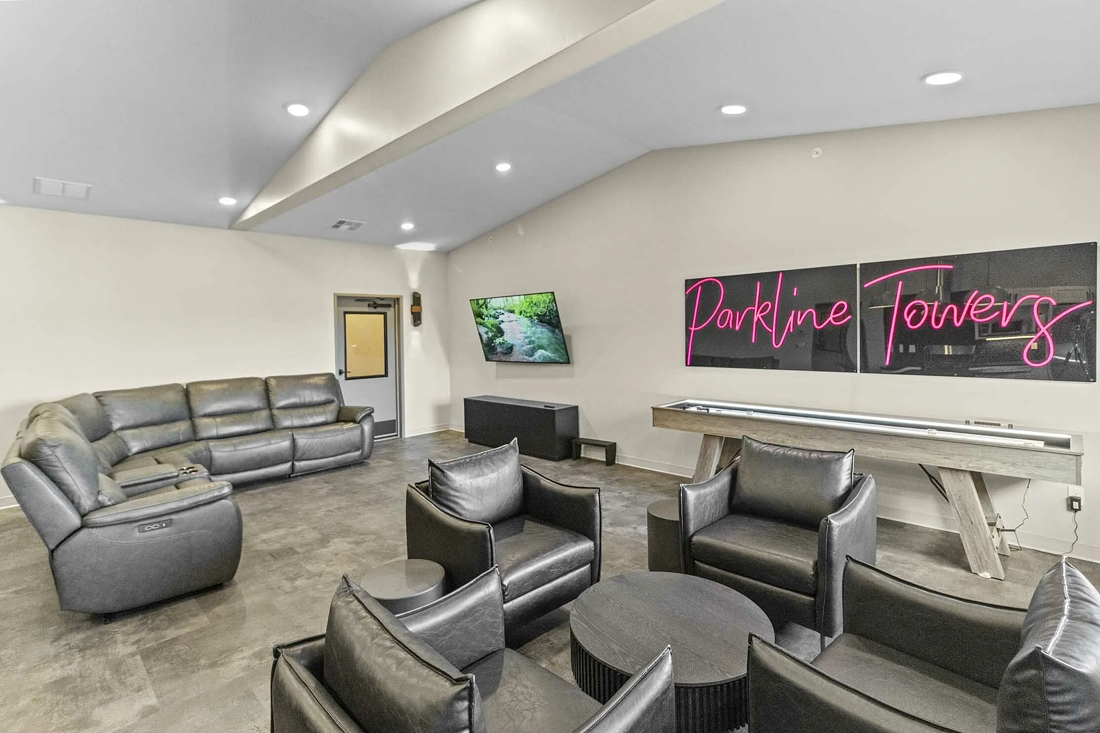 Chic and modern lounge area at Parkline Towers featuring a luxurious leather sectional sofa, stylish armchairs, and vibrant neon signage, perfect for relaxation and entertainment.