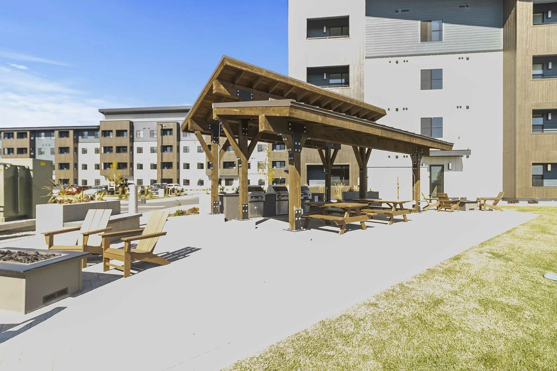 Modern apartment complex featuring a spacious outdoor area with wooden pergola, picnic tables, and cozy seating for community gatherings.