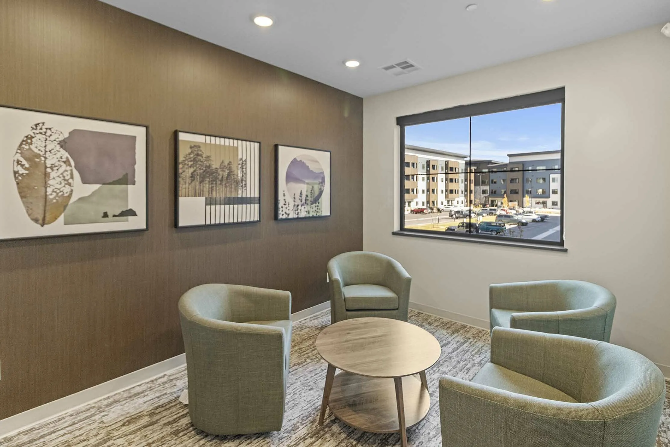 Modern apartment lounge with chic armchairs, textured walls adorned with abstract art, and a view of stylish apartment buildings through a large window.