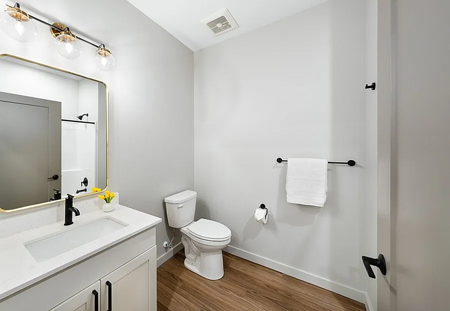 Modern bathroom showcasing elegant fixtures, a sleek white vanity, warm wood flooring, and soft ambient lighting.
