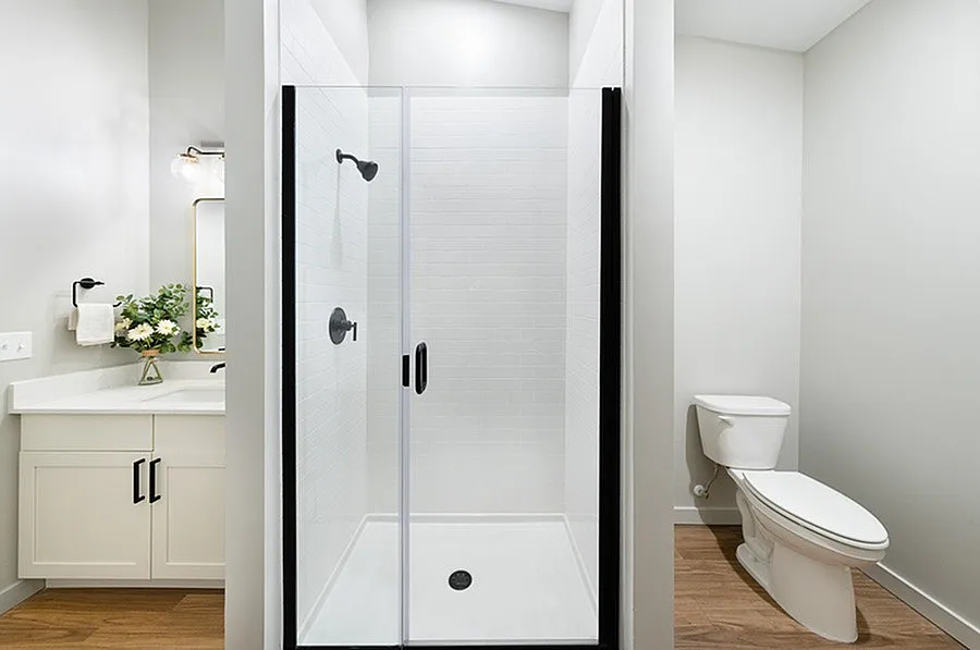 Modern bathroom featuring a sleek walk-in shower, elegant vanity with flowers, and a pristine toilet set against stylish flooring.