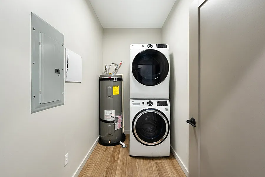 Modern laundry room with stacked washer and dryer, sleek water heater, and elegant wooden flooring.
