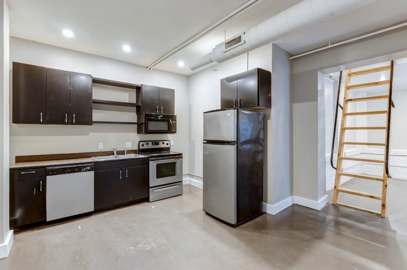 Modern kitchen with sleek dark cabinets, stainless steel appliances, and a convenient ladder to a loft space, perfect for stylish living.