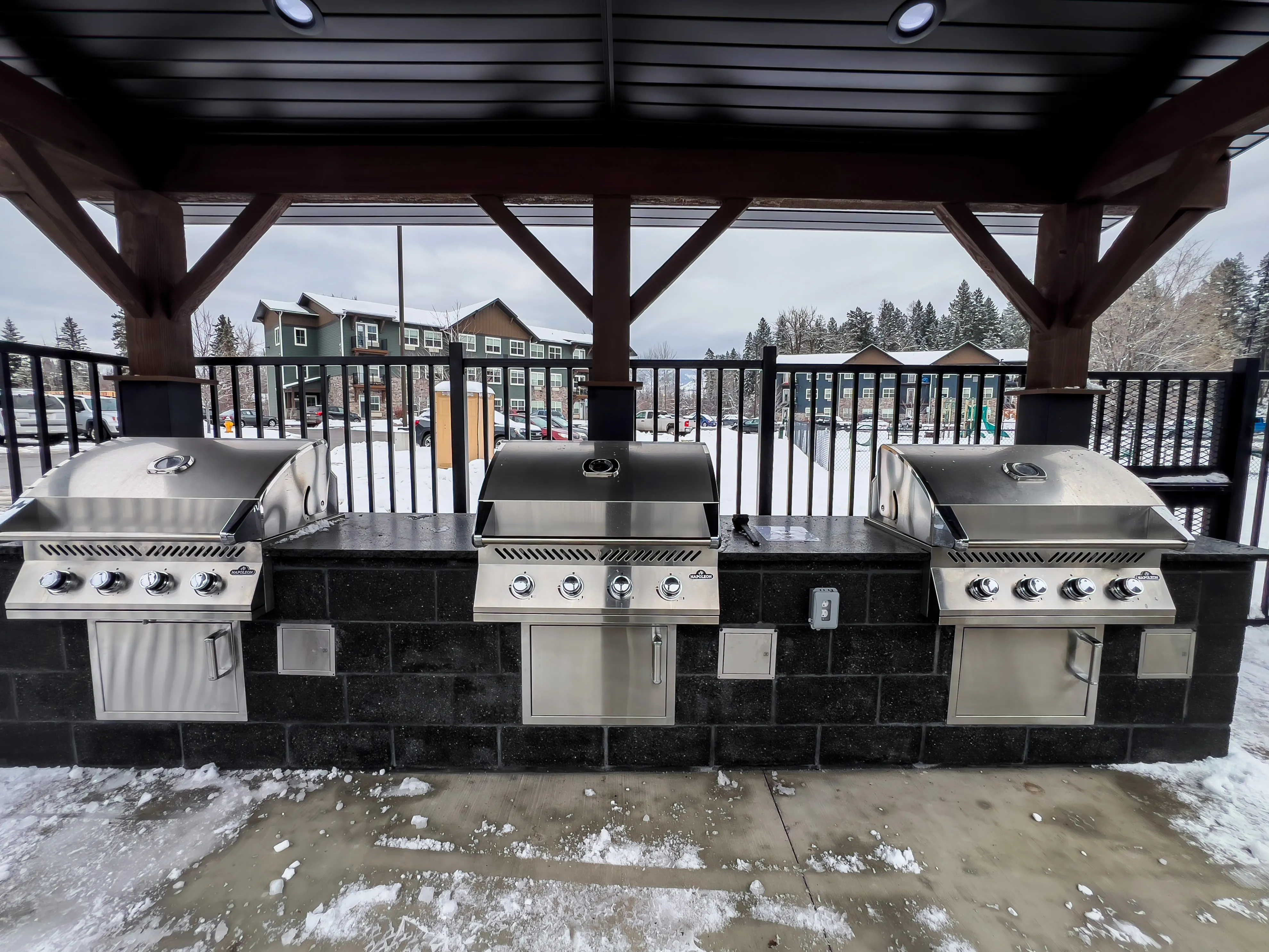 Elegant outdoor BBQ facility with three modern grills on a snowy day.