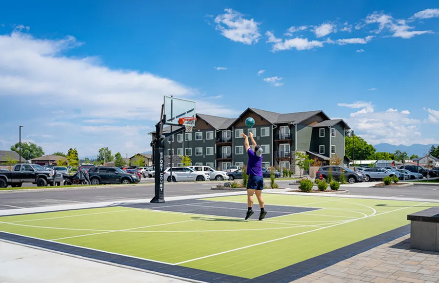 Vibrant apartment complex featuring a modern basketball court, surrounded by lush greenery and mountain views for active living.