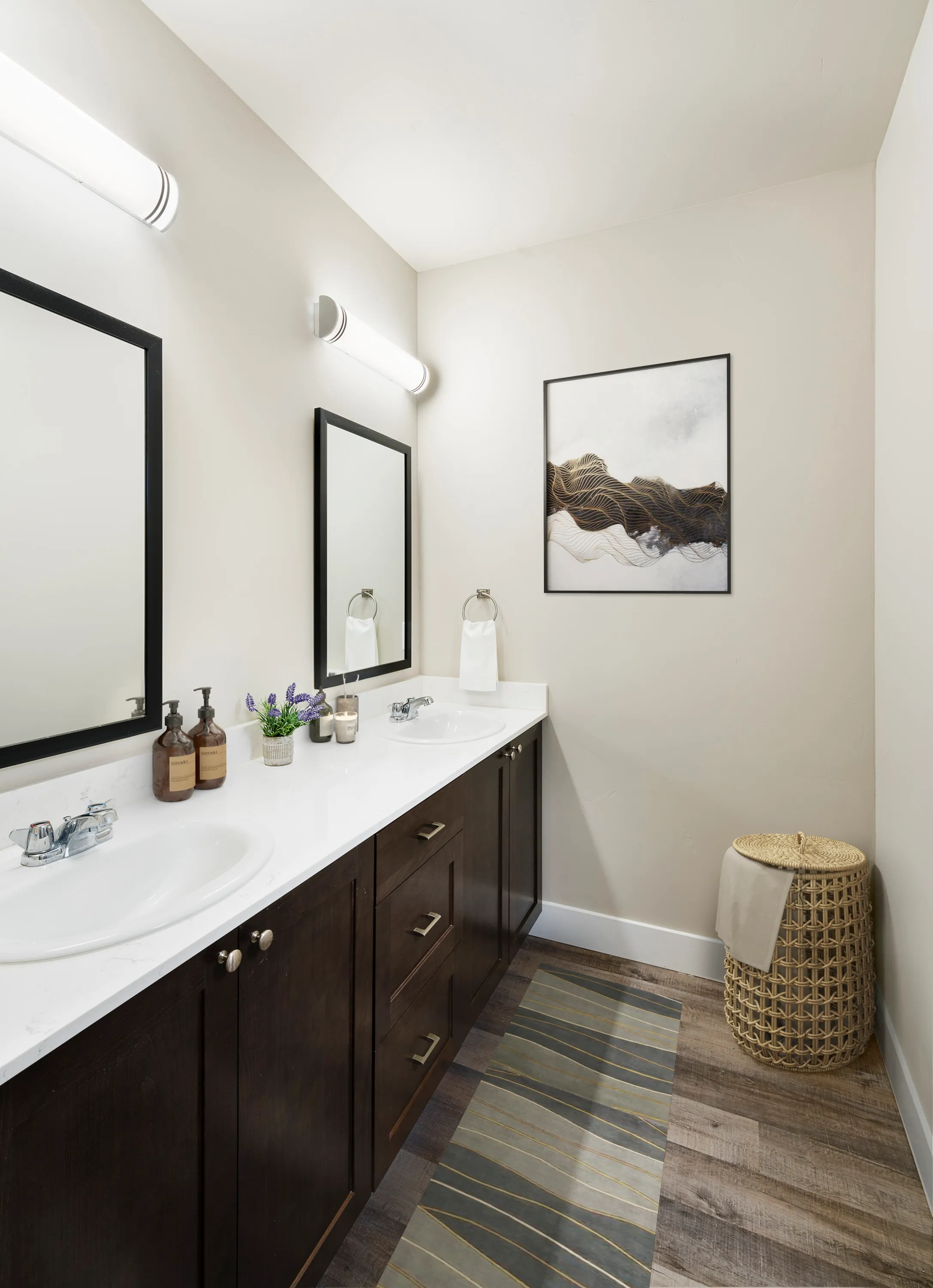 Modern bathroom with dual sinks, sleek dark cabinetry, stylish wall art, and ambient lighting, exuding elegance and sophistication.