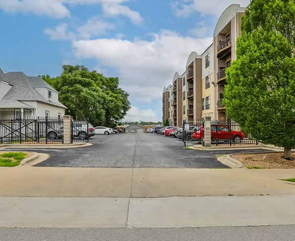 Inviting apartment complex with modern architecture, lush greenery, and ample parking space under a bright blue sky.