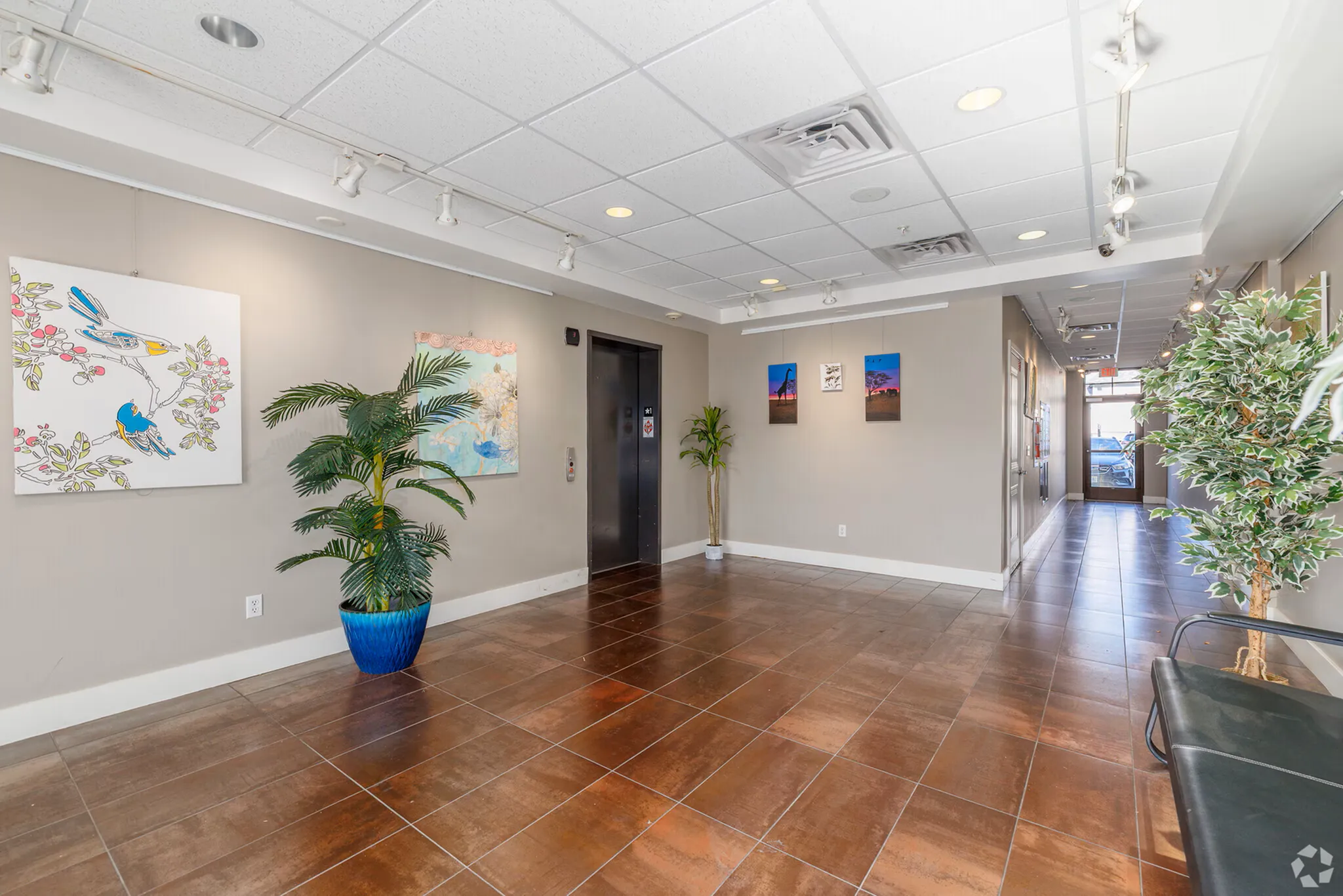Bright and inviting apartment lobby with elegant tile flooring, contemporary art, and lush green plants creating a welcoming atmosphere.