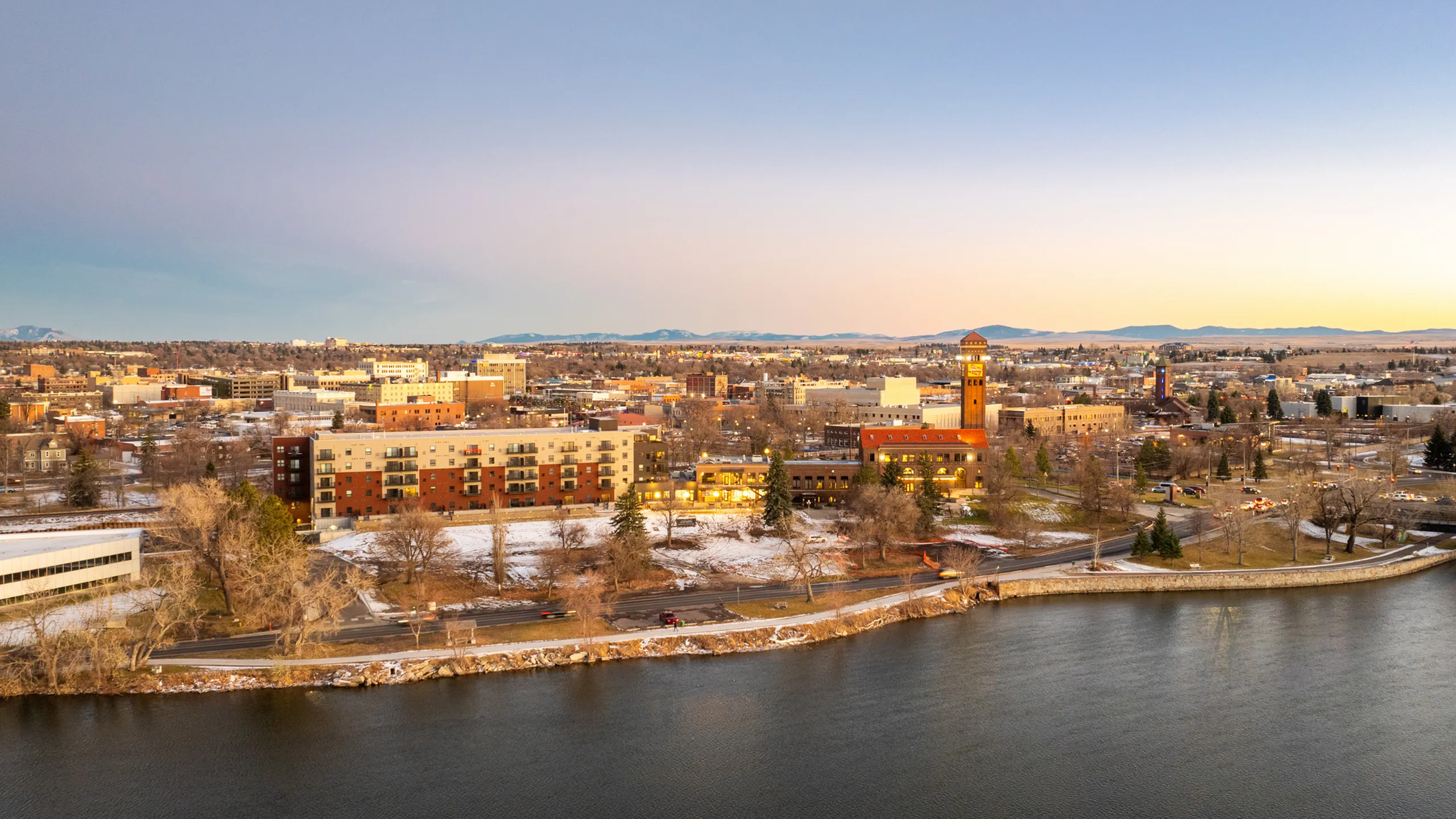 Aerial view of a vibrant cityscape with buildings, a clock tower, and a river at sunset.