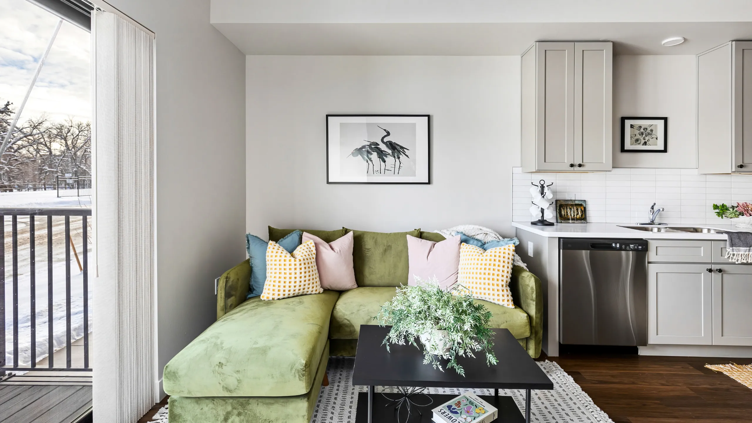 Bright and cozy living room with a green sofa, vibrant pillows, and modern kitchen.