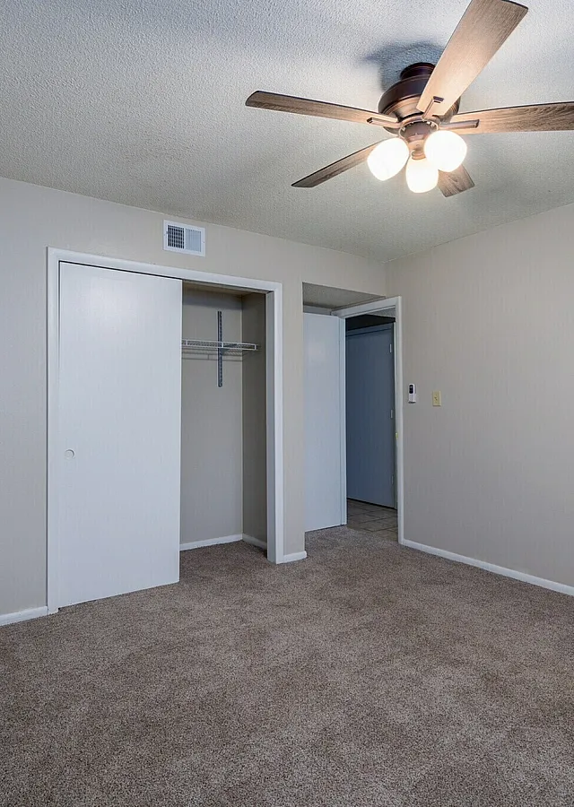 Spacious bedroom featuring a ceiling fan, plush carpeting, and a generous closet space in a modern apartment.