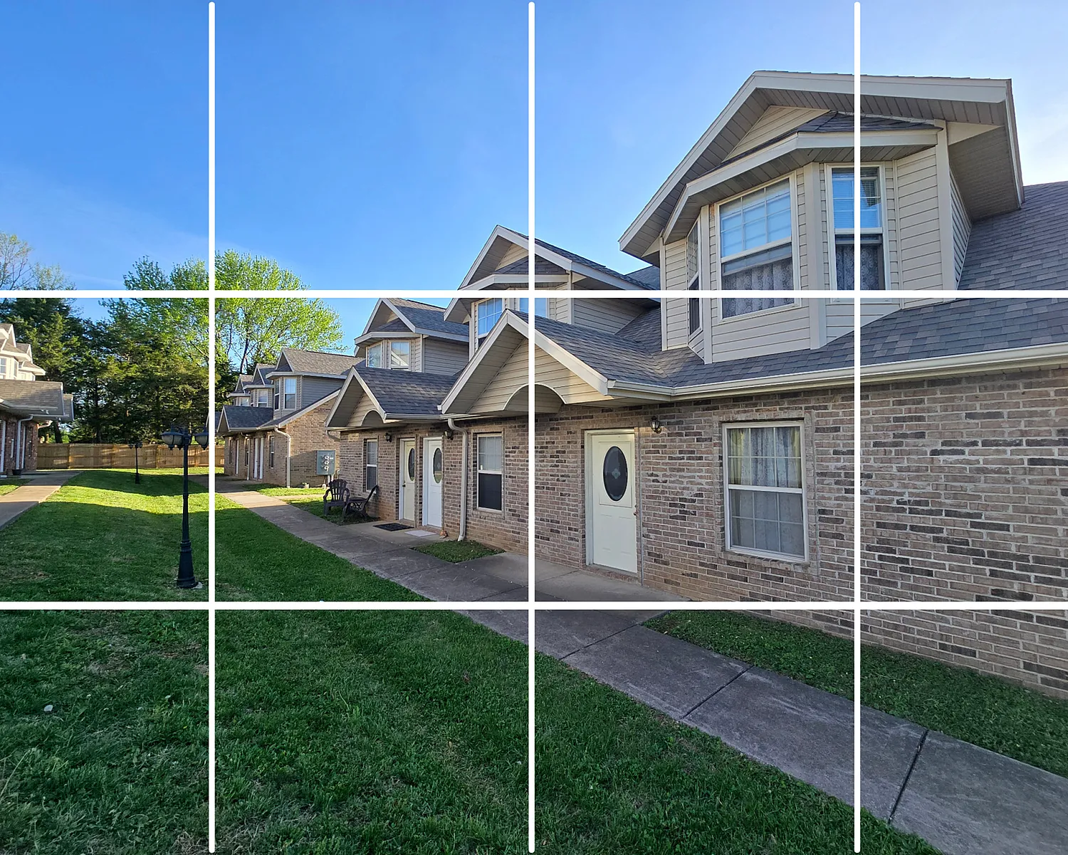 Charming townhouse exteriors with brick facades, nestled in a serene community with lush green lawns and bright blue skies.