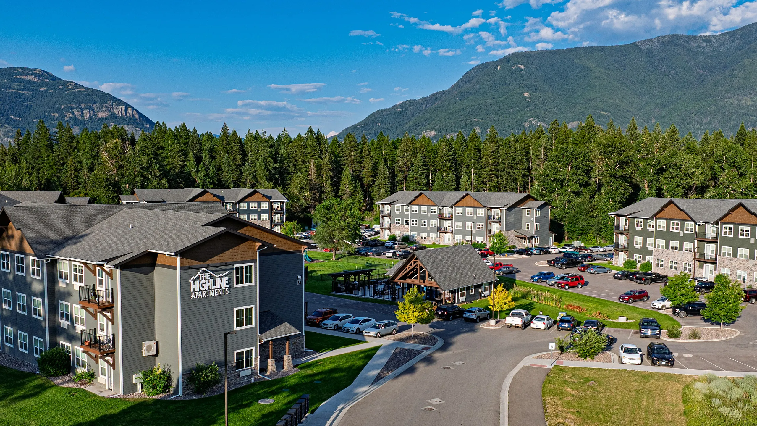 Scenic view of The Highline Apartments surrounded by lush greenery and majestic mountains, offering a serene living environment with ample parking and modern architecture.