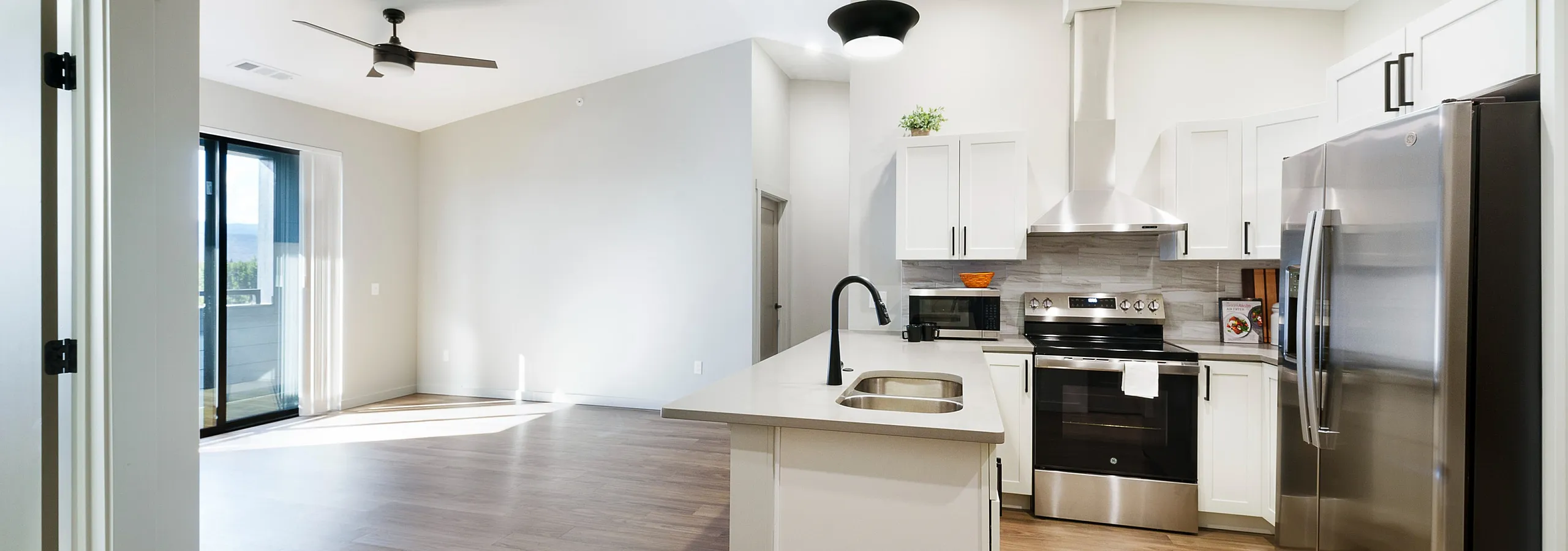Modern open-concept kitchen and living space with sleek stainless steel appliances, chic white cabinetry, and expansive hardwood floors leading to a bright living area.