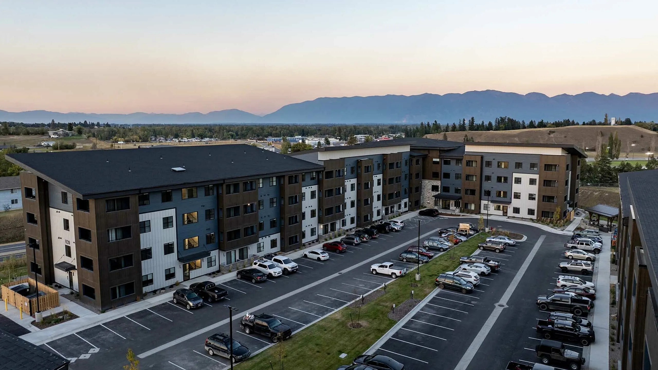 Contemporary apartment complex with four stories, ample parking, and stunning mountain views at sunset.