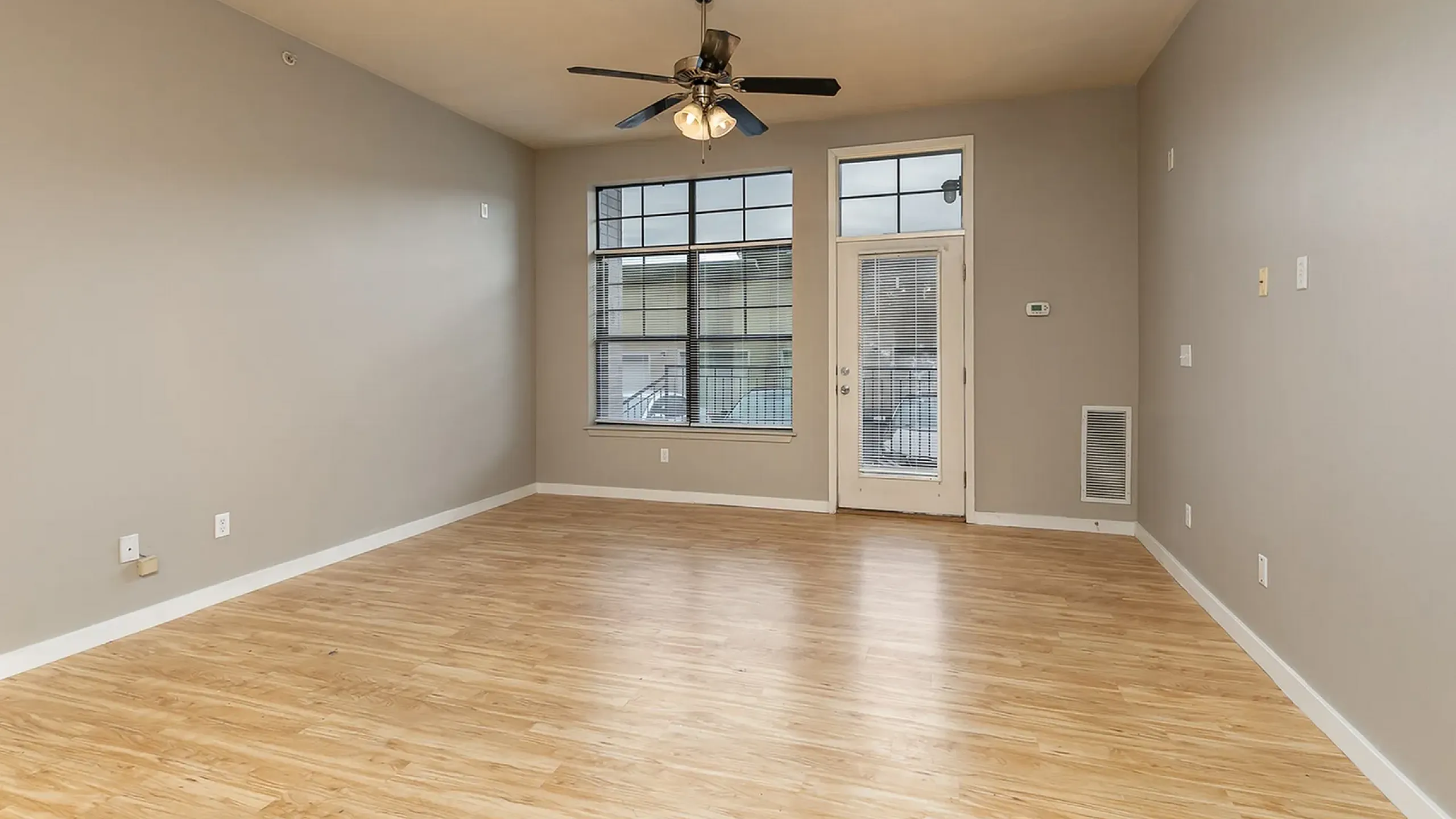 Modern living room with elegant wood flooring, neutral walls, large windows for natural light, and a stylish ceiling fan.