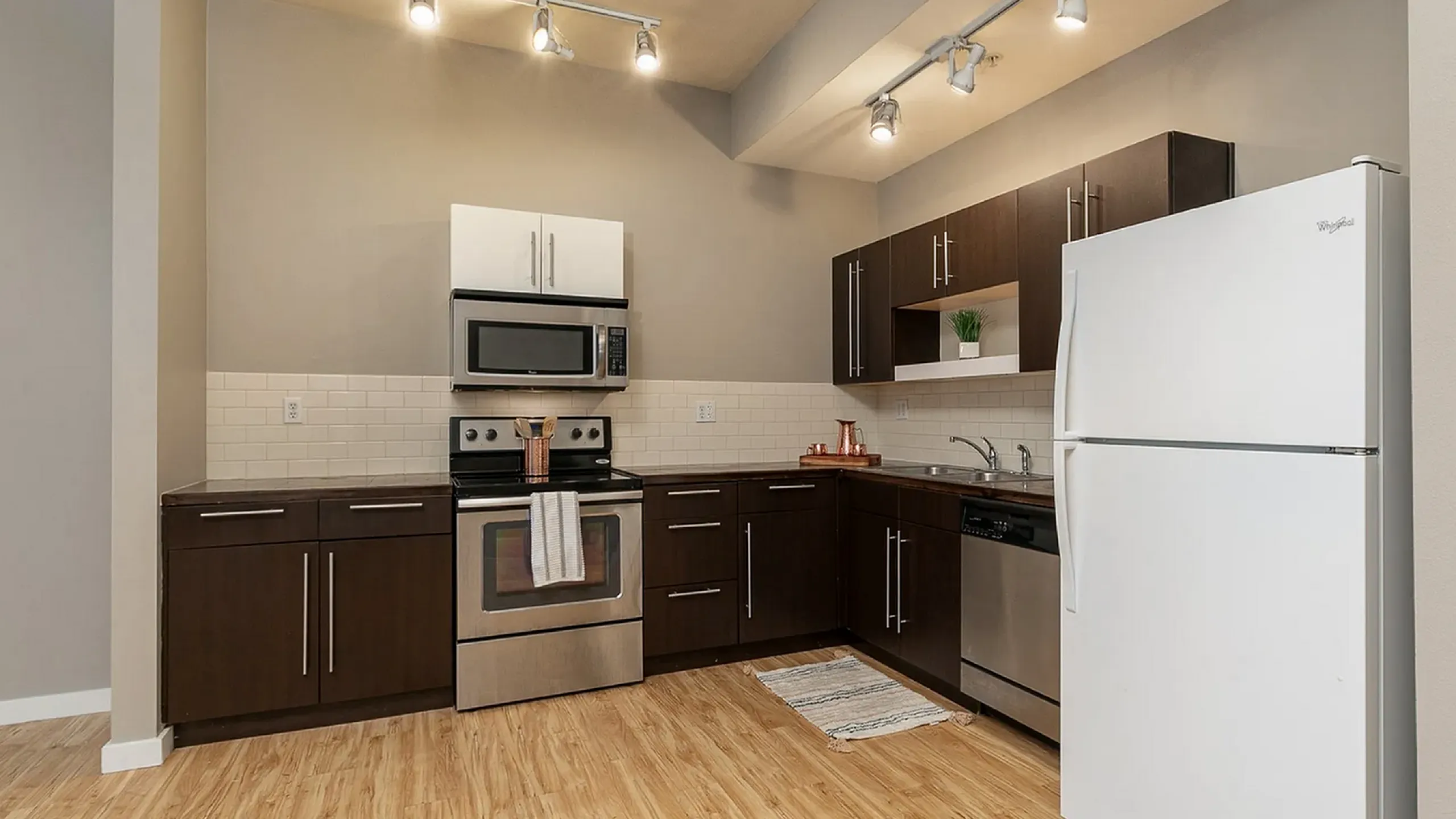 Modern kitchen with sleek dark wood cabinets, stainless steel appliances, elegant lighting, and a spacious layout.
