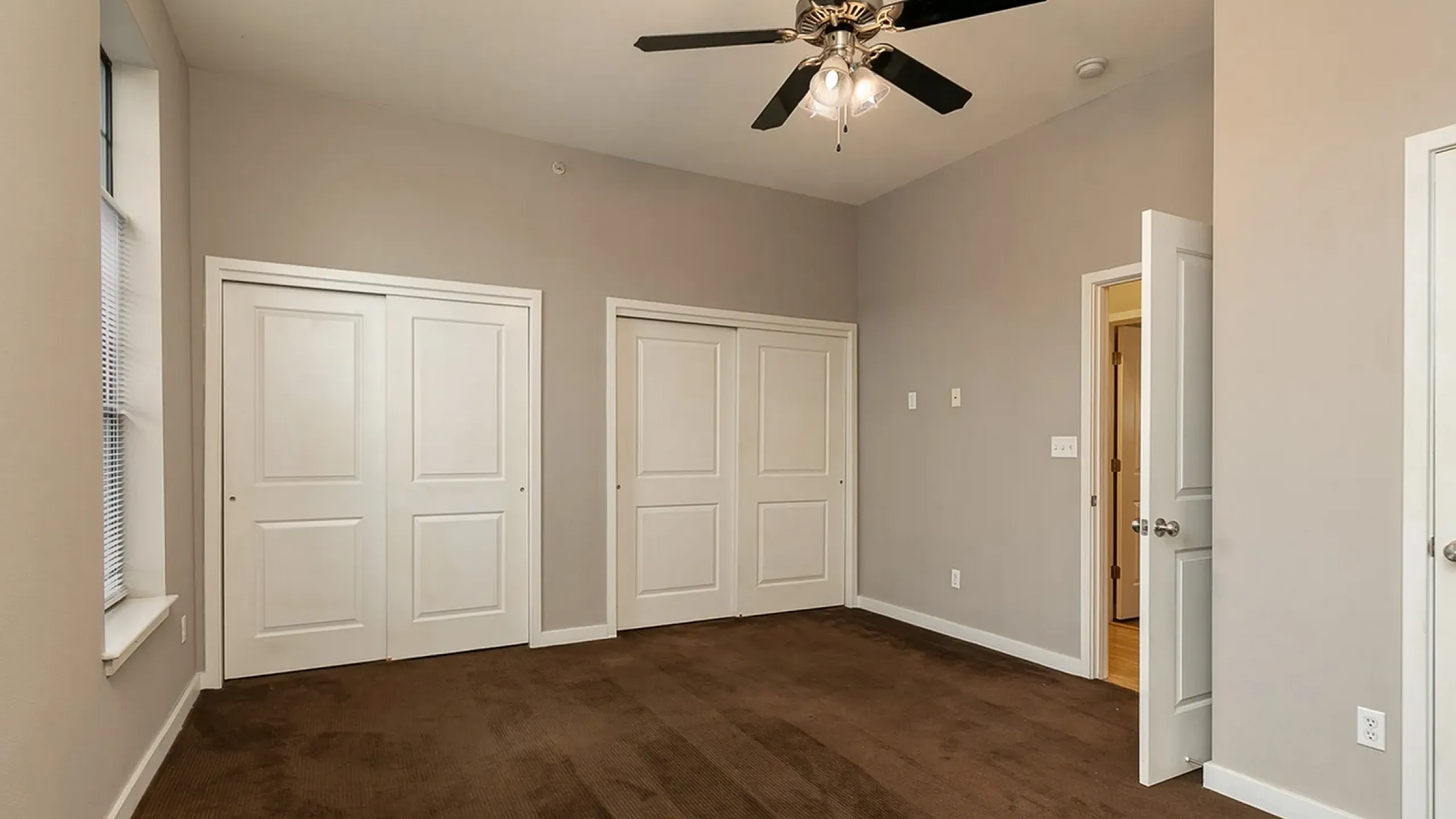 Spacious bedroom with dual closets, neutral decor, and elegant ceiling fan, offering a cozy and functional retreat.