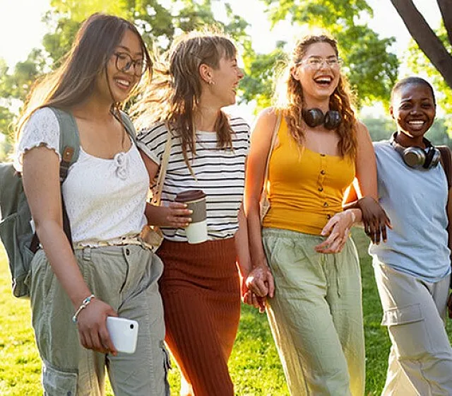 A photo of four women walking with linked arms