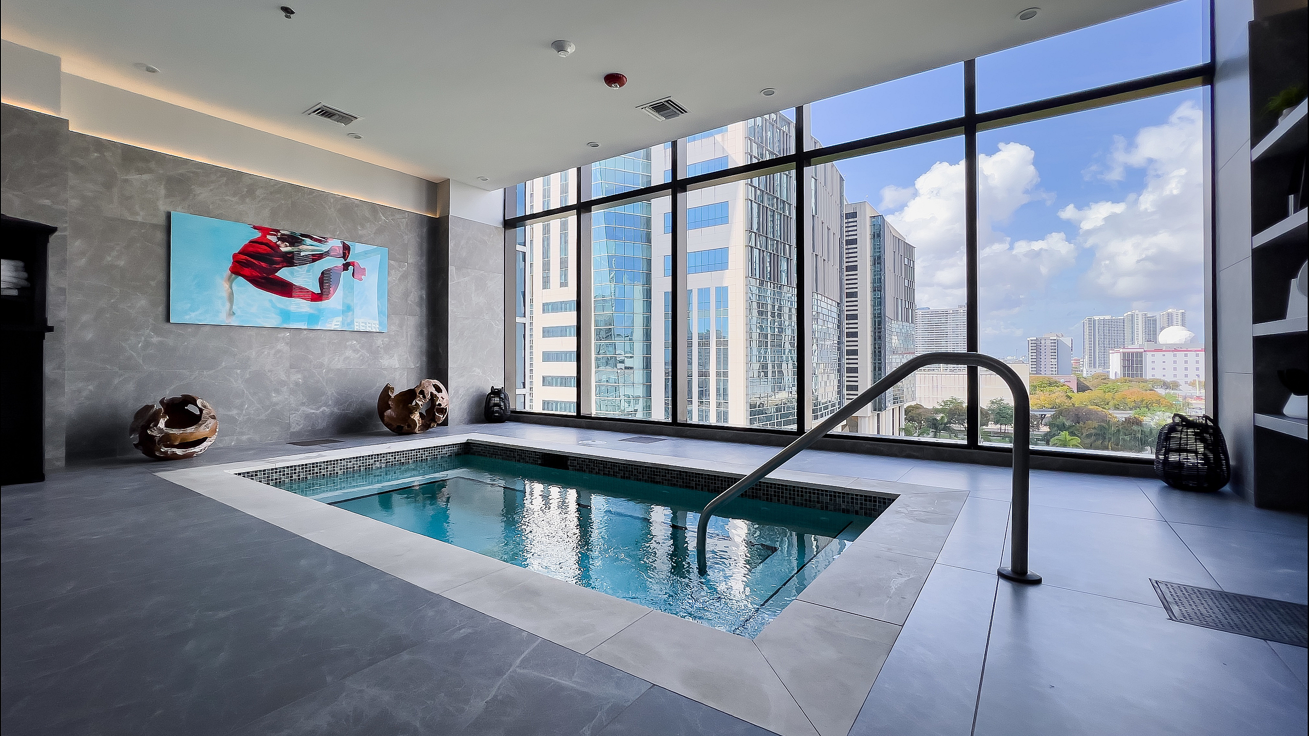Luxurious apartments in downtown Miami with indoor spa area with floor-to-ceiling windows offering stunning city views, modern art, and elegant decor.