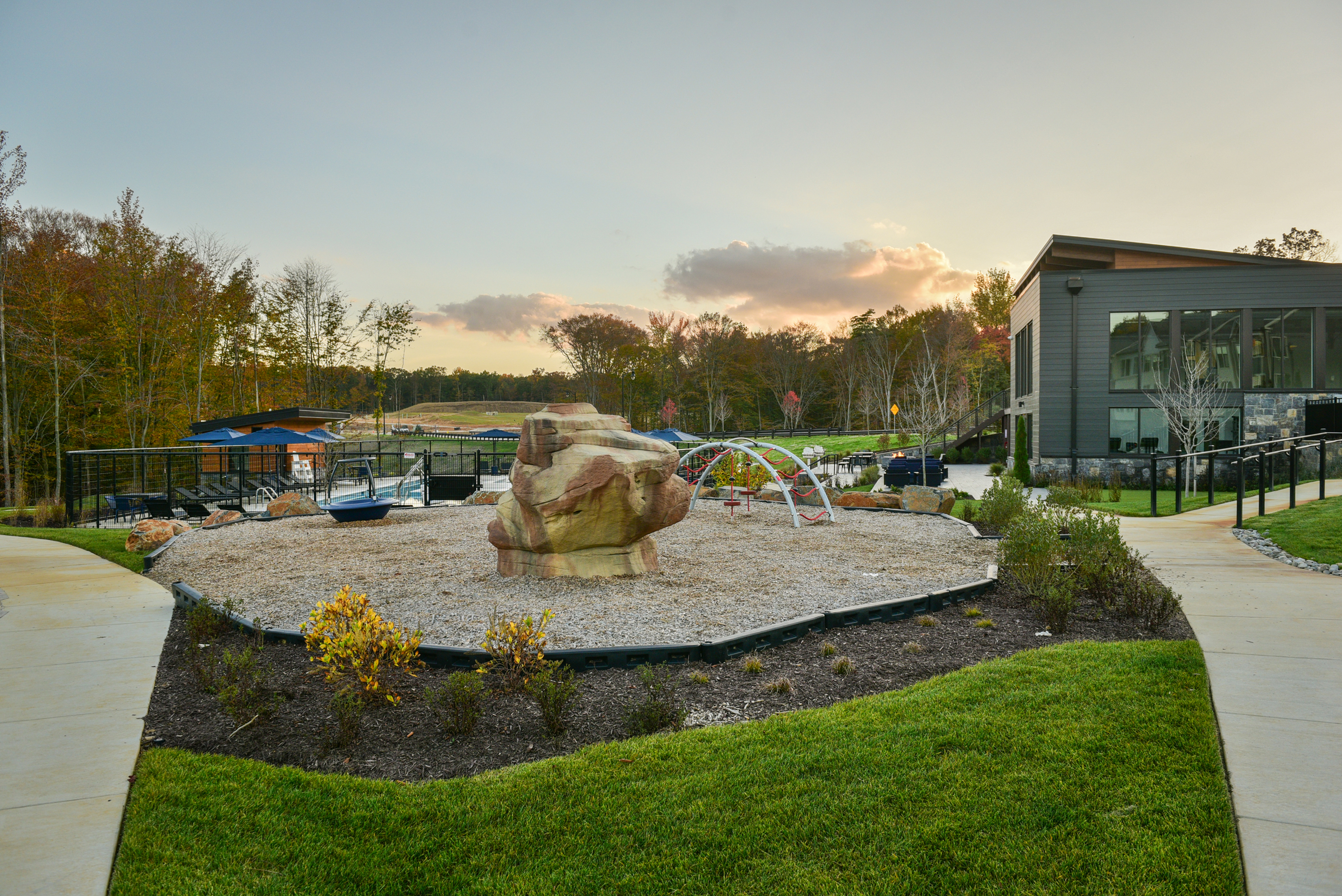 Charming outdoor recreational area with modern play equipment, set against a backdrop of beautiful fall foliage and contemporary architecture.
