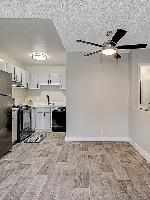 Sleek modern kitchen with black appliances and open floor space, featuring light wood flooring and a ceiling fan.