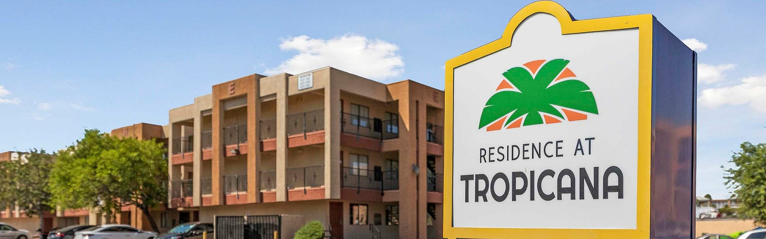 Exterior view of the Residence at Tropicana showcasing lush greenery, a welcoming entrance, and ample parking.